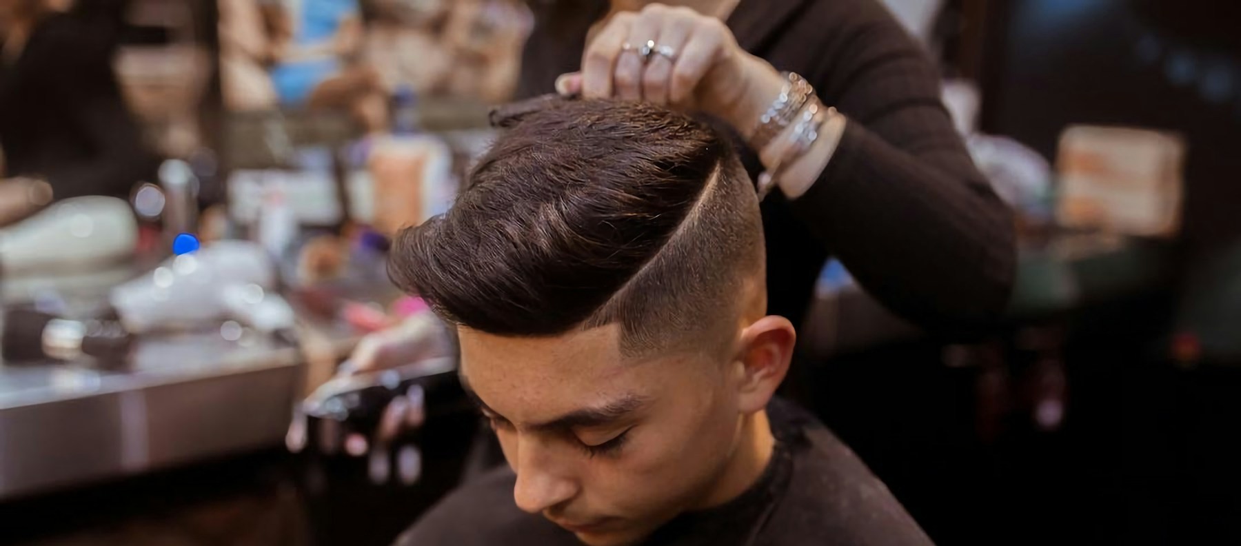Corte clásico con raya lateral y fade terminado, con el estilista dando el toque final en el interior de la barbería